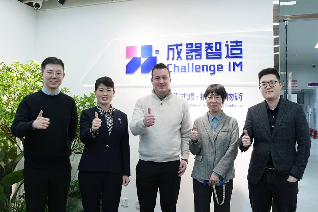 Five business professionals giving thumbs up in office with Challenge IM logo on wall