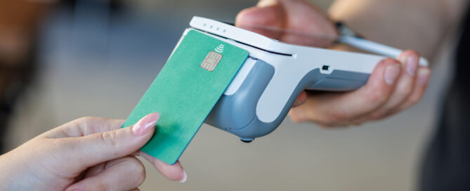 Close-up of a contactless payment using a green credit card and a modern card reader.