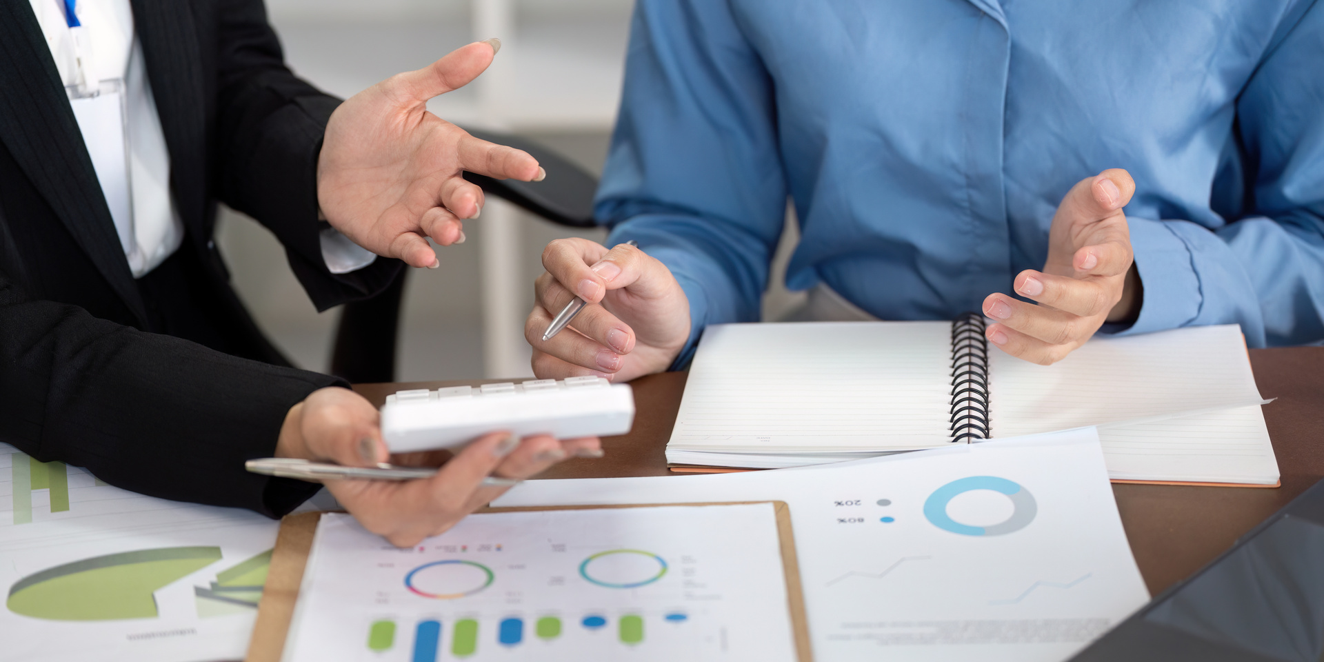 Financial Advisor Presenting Investment Options to Client Two business professionals in consultation discussing invoice finance options, with financial charts and documents spread across a modern office desk,