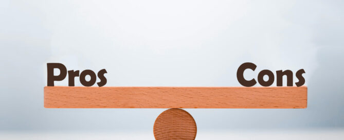 Wooden seesaw balanced on a circular fulcrum with "Pros" on the left side and "Cons" on the right side.