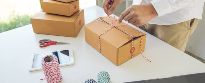 Small business owner packing product orders at workspace with laptop and shipping supplies