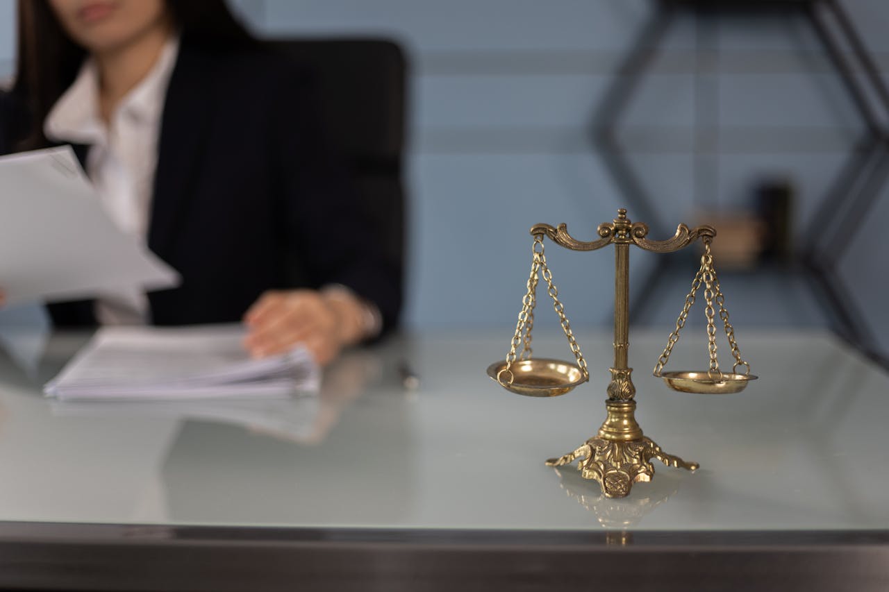 pros and cons Brass balance scale on a desk with a blurred businesswoman reviewing documents in the background.